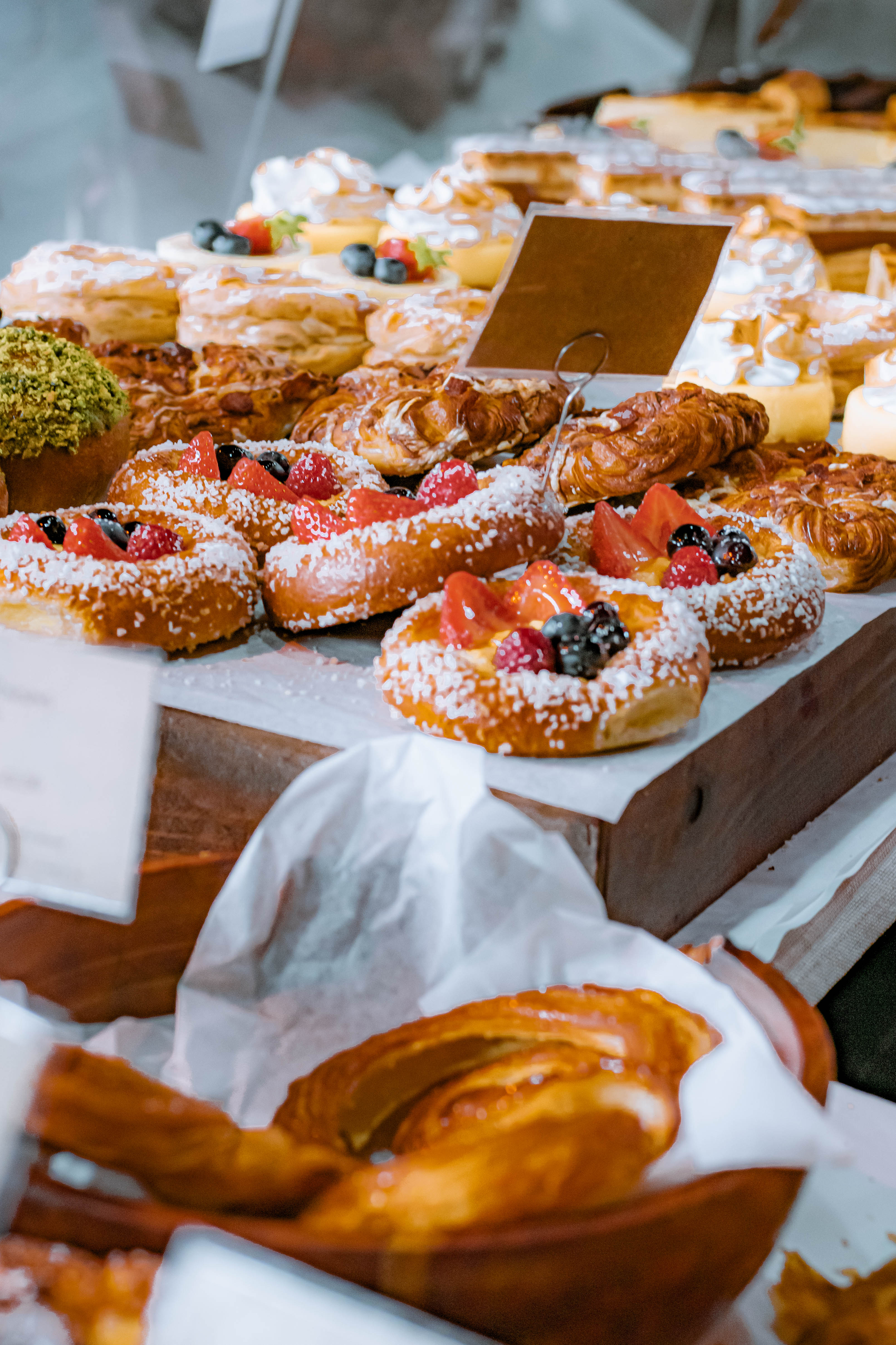 Selection of freshly baked fruit pastries and croissants with powdered sugar topping at Comptoir Bakery, including danishes with strawberries, blueberries, and raspberries at the market stall.