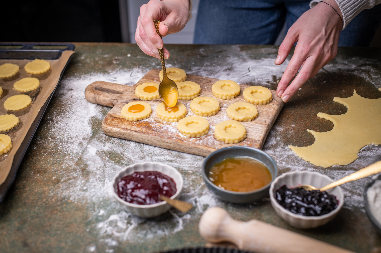 Person preparing cookies with jam and cream on a wooden board