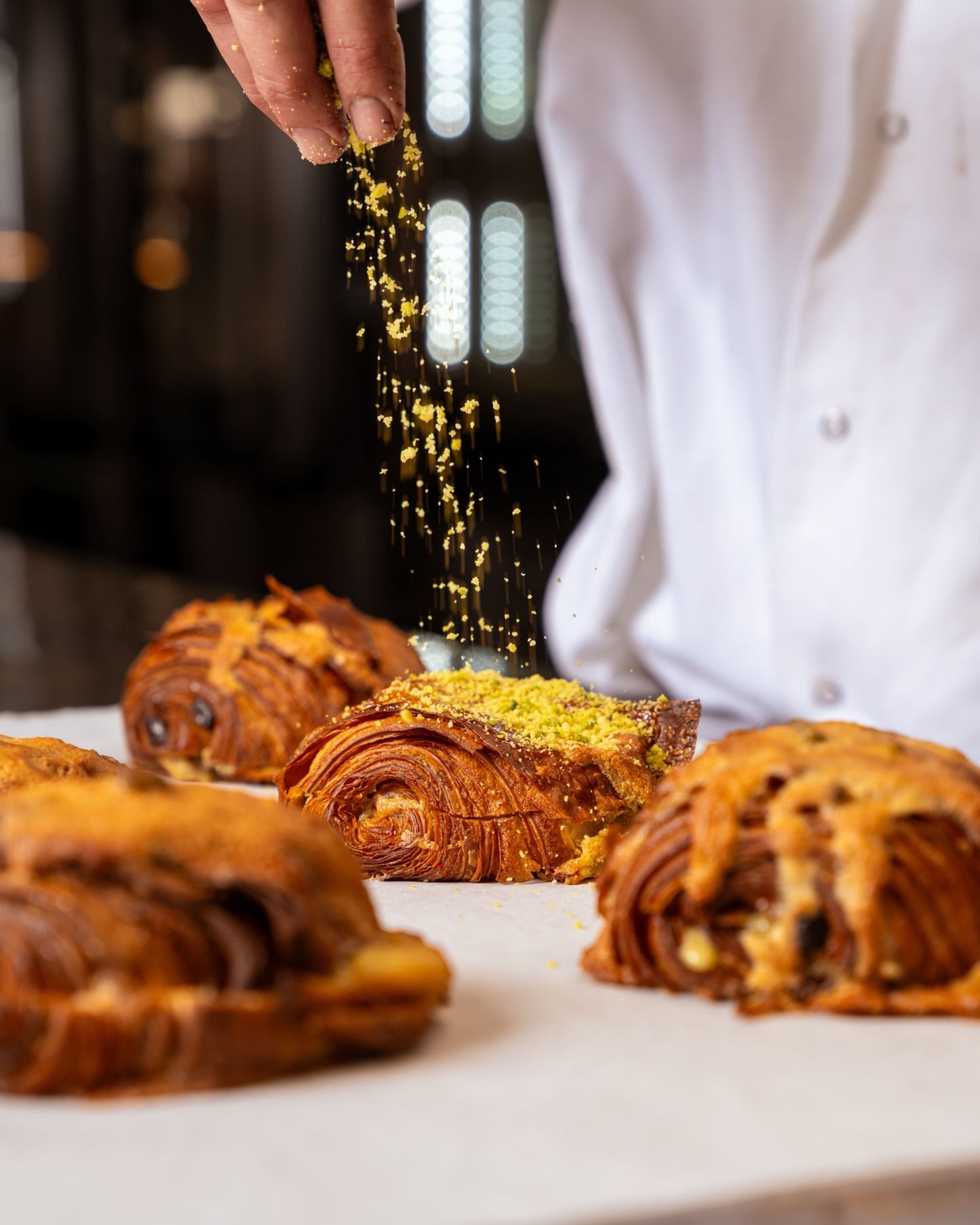 chef sprinkling pistachio nuts onto pastries